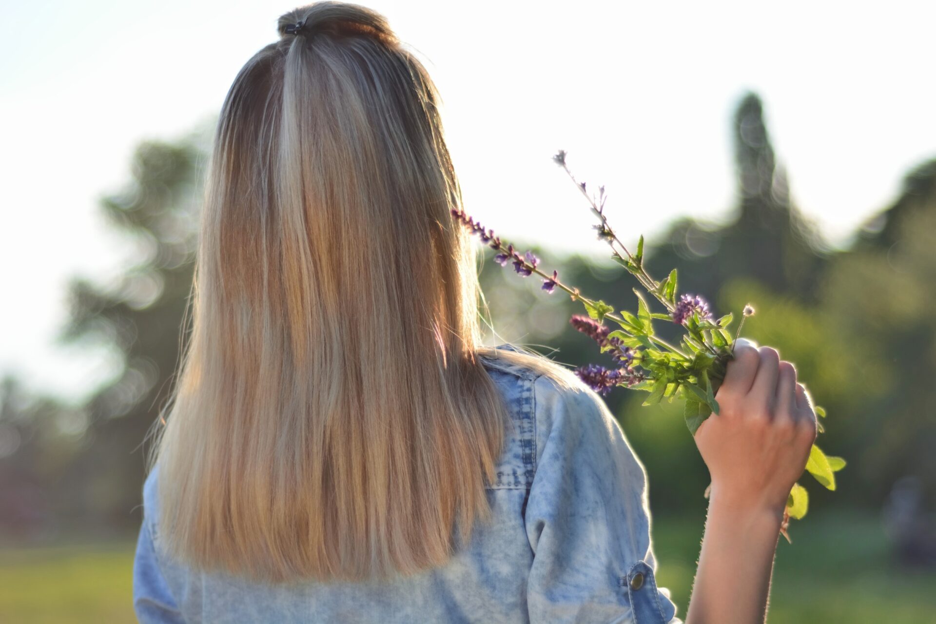 A woman with blonde hair that lightens towards the ends stands with a lavender bouquet in her hand.